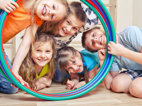 Fünf fröhliche Kinder schauen durch Hula Hoop Reifen