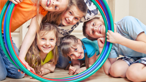 Fünf fröhliche Kinder schauen durch Hula Hoop Reifen
