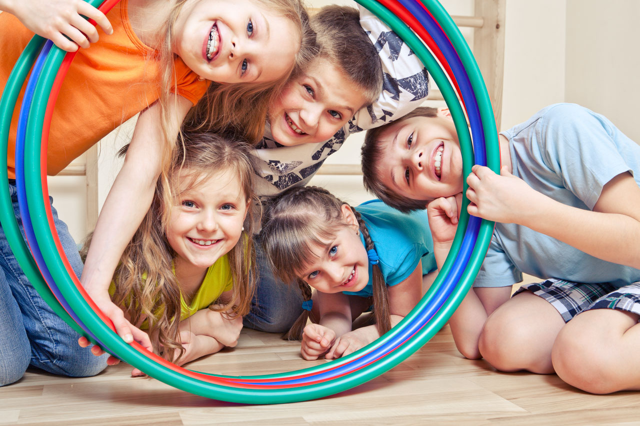 Fünf fröhliche Kinder schauen durch Hula Hoop Reifen